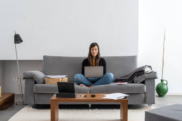 Nuori nainen kannettavan tietokoneen televiestinnän sohvalla kotonaan
 - Valokuva, kuva