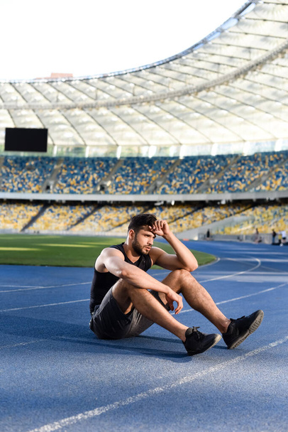 Stadyumdaki koşu pistinde dinlenen yorgun yakışıklı sporcu. - Fotoğraf, Görsel