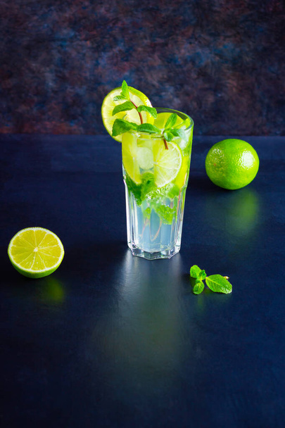 Mojito cocktail with lime and mint in tall glass. Fresh mojito in glass on a dark background. Refreshing mint cocktail with lime. Infused water. Copy space - 写真・画像