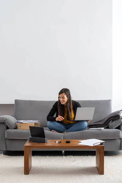 Mujer joven con ordenador portátil y tableta de teletrabajo en el sofá en su casa
 - Foto, imagen