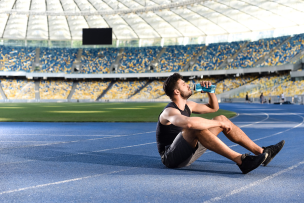 apuesto deportista descansando y agua potable en pista en el estadio
 - Foto, Imagen