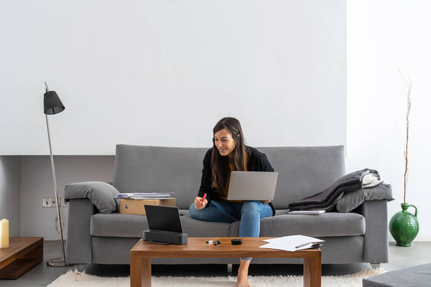 Nuori nainen, jolla on kannettava tietokone ja tabletti televiestintä sohvalla kotonaan
 - Valokuva, kuva