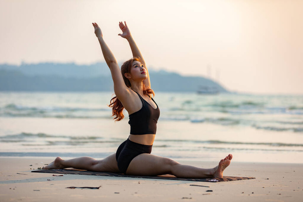 Asiatique jeune femme pratique Yoga Singe Dieu Pose ou Yoga Hanumanasana pose sur le sable et la plage avec coucher de soleil belle mer dans l'île tropicale, Se sentir à l'aise et se détendre en vacances, Concept de yoga vacances
 - Photo, image