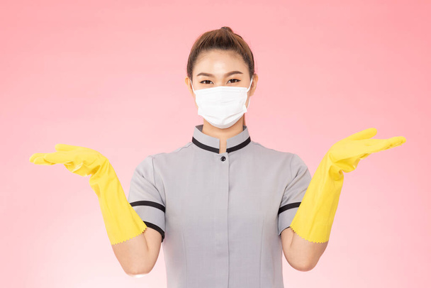Attractive Beautiful Asian woman maid wearing face mask and gloves smile and open palm sign for display product feeling so happiness and confident,Isolated on pink background,Cleaning Service concept - 写真・画像