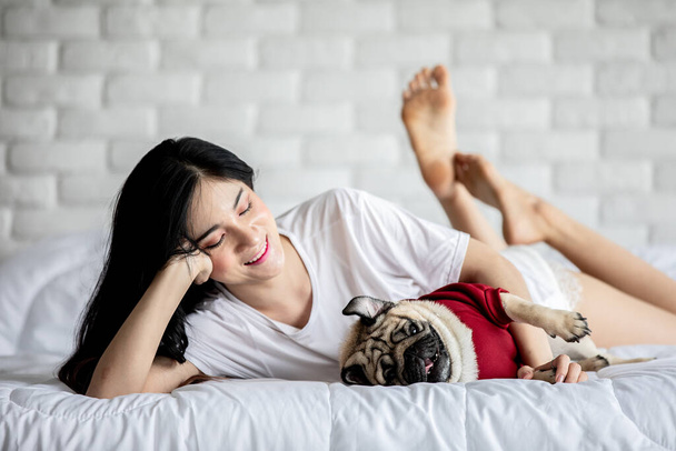Beautiful Asian young woman playing with her dog and smile with dog pug breed looking in funny and serious face in bedroom feeling so happiness and relaxation,Dog Friendship Concept - Foto, Imagen