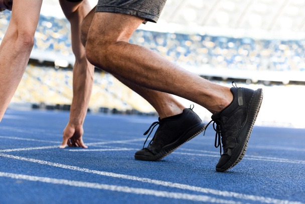cropped view of runner in start position on running track at stadium - Foto, afbeelding