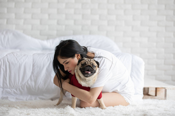 Beautiful Asian young woman playing with her dog and smile with dog pug breed looking in funny and serious face in bedroom feeling so happiness and relaxation,Dog Friendship Concept - Foto, afbeelding