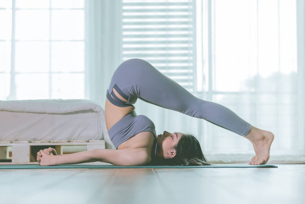 Attractive Asian woman practice yoga Halasana pose or plow pose to meditation in bedroom after wake up in the morning with warm light Feeling so comfortable and relax,Healthcare Concept - Foto, Bild