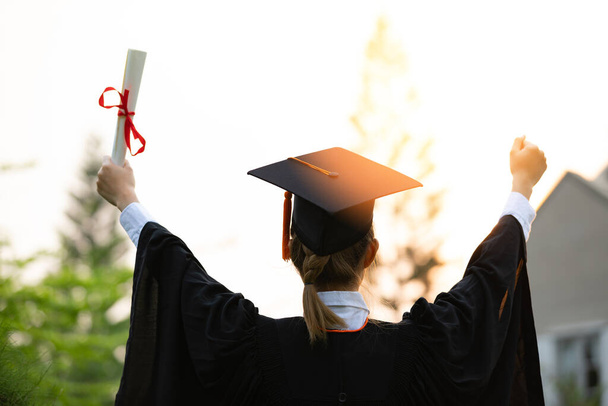 Arrière de la vue Diplômée mettre les mains en l'air et célébrer avec certificat dans sa main et si fière et le bonheur dans le jour du commencement, Félicitations de l'élève dans le jour de la remise des diplômes, Concept de réussite scolaire
 - Photo, image