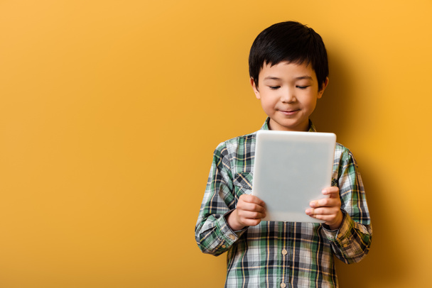 słodkie uśmiechnięty Azji chłopiec za pomocą cyfrowy tabletka na żółty - Zdjęcie, obraz