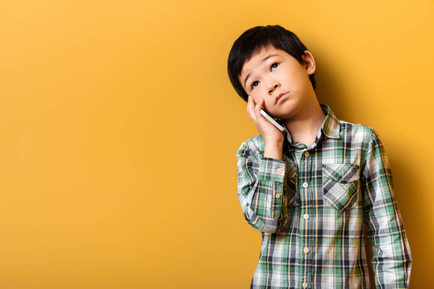 chico asiático triste hablando por teléfono inteligente en amarillo - Foto, Imagen