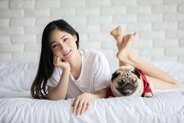 Beautiful Asian young woman playing with her dog and smile with dog pug breed looking in funny and serious face in bedroom feeling so happiness and relaxation,Dog Friendship Concept - Foto, Bild