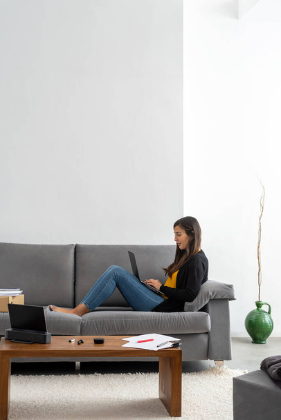 Mujer joven con portátil teletransportarse en el sofá en su casa
 - Foto, imagen