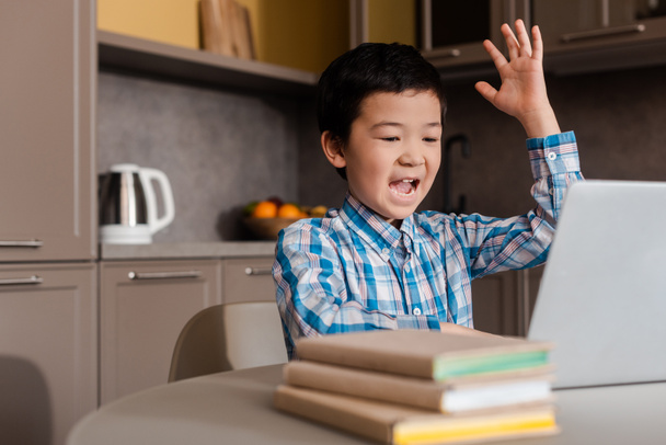 emocjonalny azjatycki chłopiec z ręka do góry krzycząc i ucząc się online z laptopem w domu podczas samoizolacji - Zdjęcie, obraz