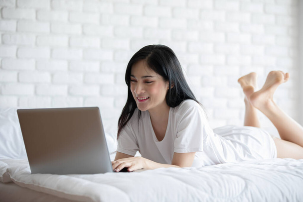 Piękne Atrakcyjne Azjatyckie młoda kobieta leżąca na łóżku i za pomocą laptopa do korzystania z mediów społecznościowych i zakupy online relaks w przytulnej sypialni na wakacjach, Styl życia w sypialni Concept  - Zdjęcie, obraz