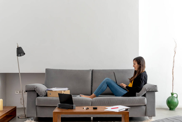 Молодая женщина с ноутбуком телекоммуникационных на диване у себя дома
 - Фото, изображение
