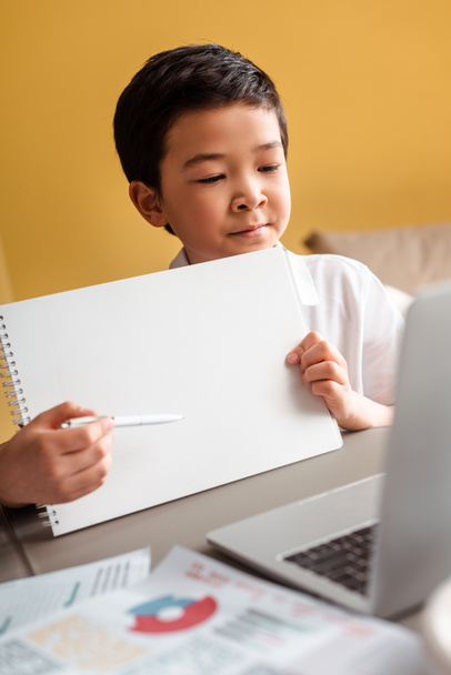 Karantina sırasında evde dizüstü bilgisayarı ve not defteriyle çalışan Asyalı yakışıklı çocuk. - Fotoğraf, Görsel