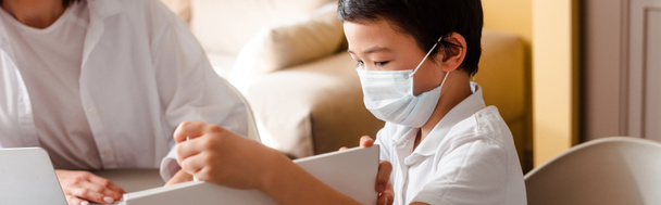asian boy in medical mask studying with mother at home on quarantine, horizontal concept - Photo, image