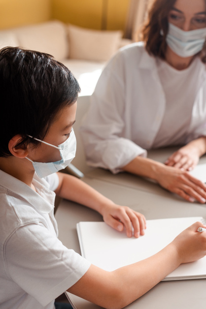 asian boy in medical mask studying with mother at home on self isolation - Foto, Imagem
