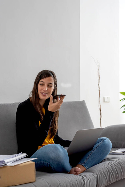 Young woman with laptop and phone telecommuting on the sofa at her home - Photo, image
