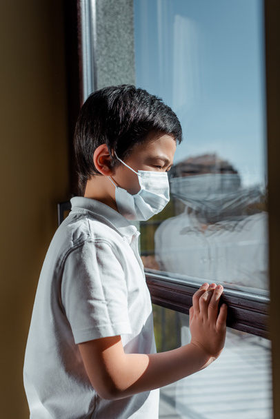 Tıbbi maskeli Asyalı çocuk karantina penceresinden bakıyor. - Fotoğraf, Görsel