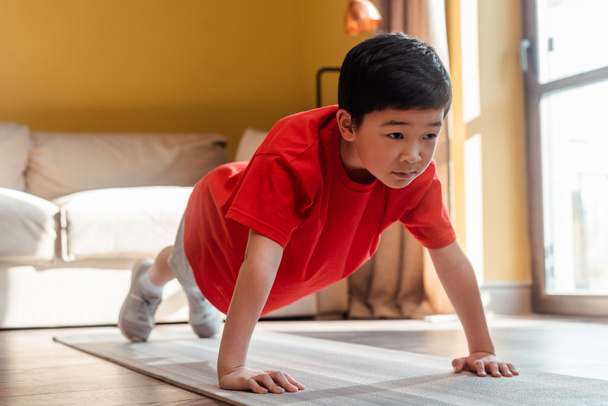 sportive asian kid doing push ups on fitness mat at home during self isolation - Фото, зображення