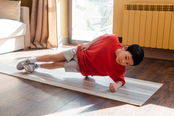 sportieve aziatische kid doen zijplank op fitness mat thuis tijdens zelf isolatie - Foto, afbeelding