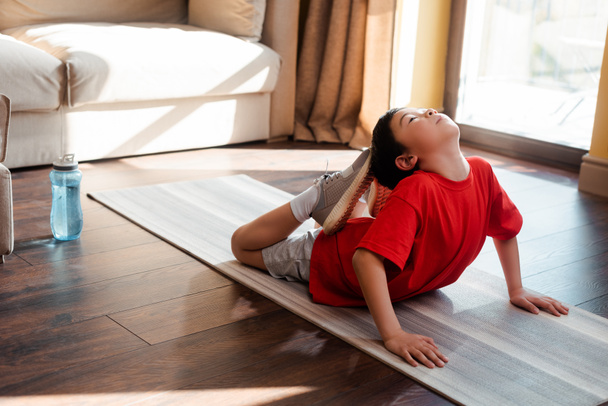 sportive asian kid stretching on fitness mat at home during quarantine - Photo, Image