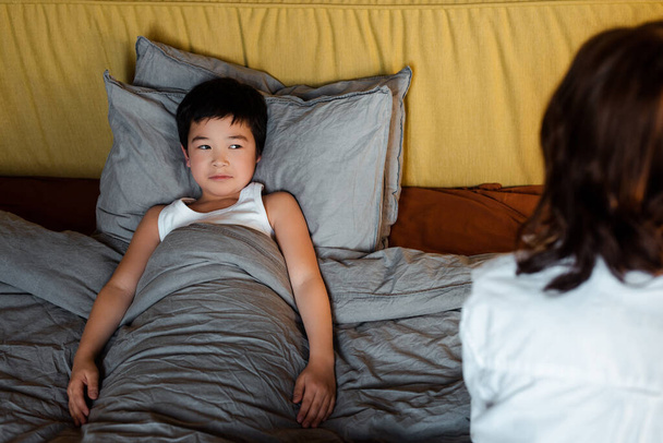 cute asian boy lying in bed with mother near on quarantine - Photo, Image