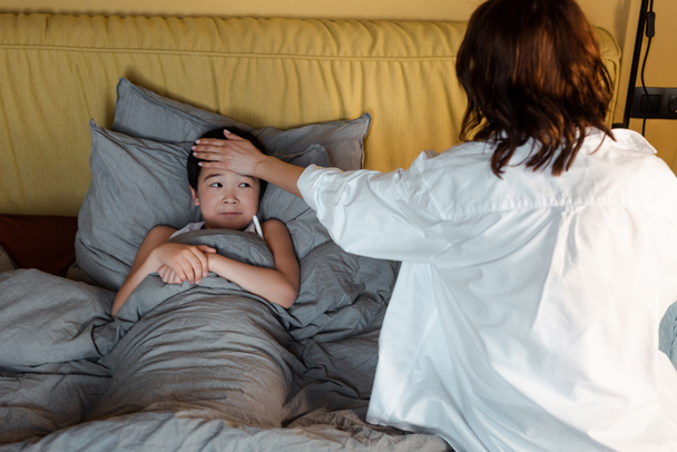 malato asiatico ragazzo avendo febbre e sdraiato a letto con madre vicino su quarantena - Foto, immagini