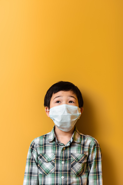 surprised asian boy in medical mask on yellow during self isolation - Foto, Bild