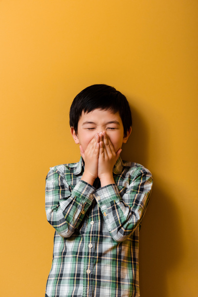 άρρωστο ασιατικό αγόρι φτερνίζεται στο κίτρινο κατά τη διάρκεια της απομόνωσης - Φωτογραφία, εικόνα