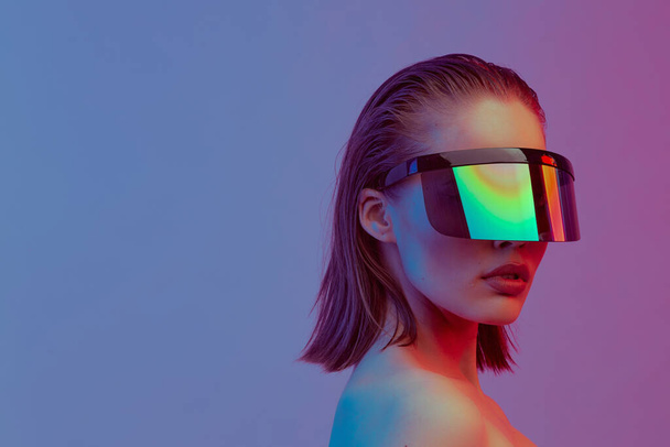 Cool stylish girl with a fashionable hairstyle and stylish glasses with a large glass poses on a bright neon background. - Foto, Bild