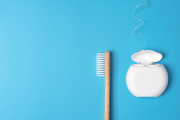 Dental floss container and bamboo toothbrush on blue background. Daily oral hygiene, teeth care and health. Cleaning products for mouth. Dental care concept. Empty place for text or logo. - Foto, imagen