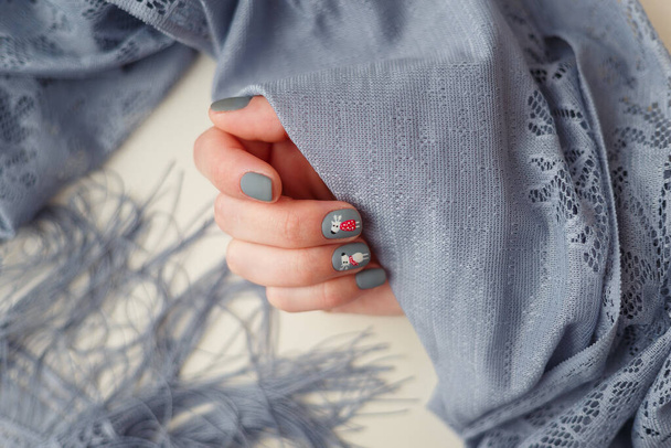 Руки женщины с рождественским маникюром оленя на ногтях, держащих серую шаль. Новый год, зимние каникулы, уход за ногтями и руками, красота и мода
. - Фото, изображение