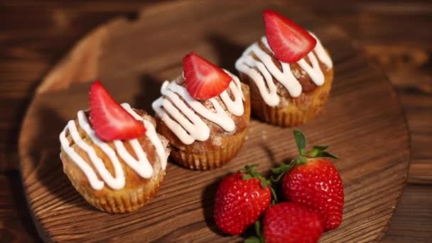 A delicious strawberry muffin lies on a wooden table, and a strawberry lies nearby. The concept of a delicious breakfast. Close-up. - Footage, Video