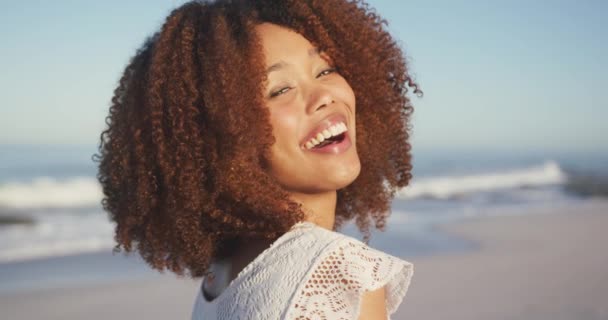 Front view of an African American woman enjoying time in the sun on a tropical beach, looking to camera and smiling, in slow motion - Кадри, відео