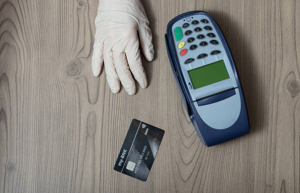 Käsi suojaava kertakäyttökäsine pankkikortilla ja pankkiautomaatilla puisessa myymälätiskillä käsite ostoksia aikana Covid-19 pandemia
 - Valokuva, kuva