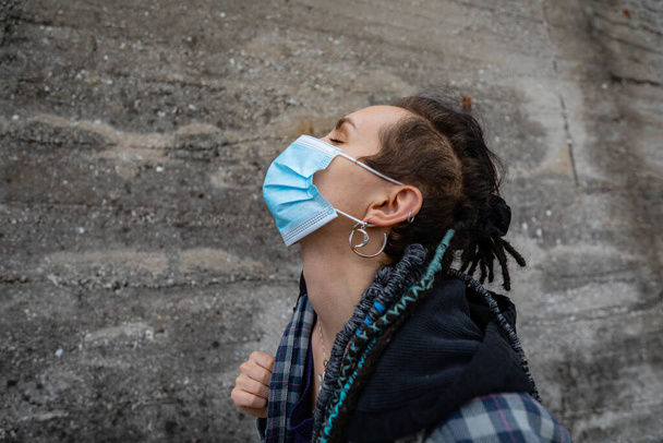 jonge punk vrouw in het midden van een betonnen stad proberen te ruiken de geur van de lucht ondanks haar beschermende masker waardoor het moeilijk voor haar om adem te halen - Foto, afbeelding