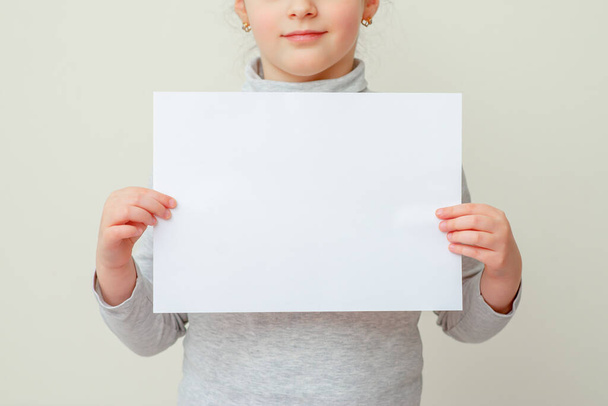 Mockup άδειο φύλλο χαρτιού στα χέρια του μικρού κοριτσιού. Το παιδί κρατά κενό φύλλο έτοιμο για μήνυμα σε κίτρινο φόντο. - Φωτογραφία, εικόνα