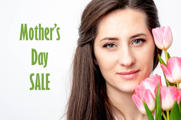 Retrato de media cara de mujer joven con tulipanes rosados sonriendo sobre fondo blanco con texto Día de la Madre Venta
. - Foto, imagen