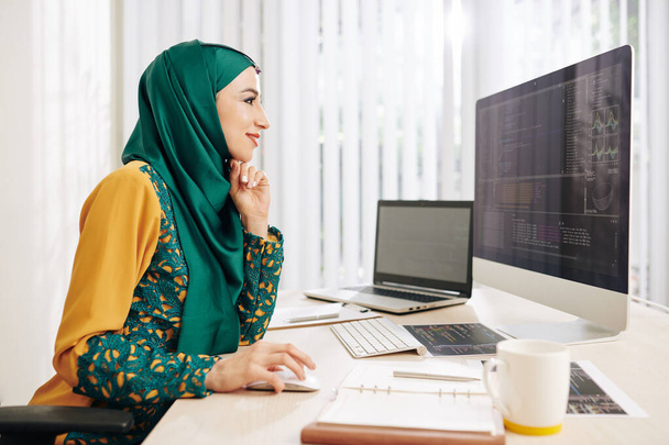 Geleneksel elbiseli gülümseyen müslüman genç kadın bilişim şirketi için yeni bir proje üzerinde çalışırken eğleniyor. - Fotoğraf, Görsel
