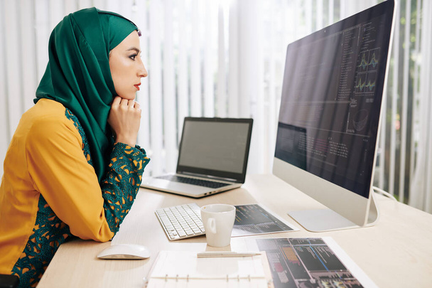 Stirnrunzeln einer ernsthaften Muslimin auf der Suche nach Fehlern in ihrem Programmiercode auf dem Computerbildschirm - Foto, Bild