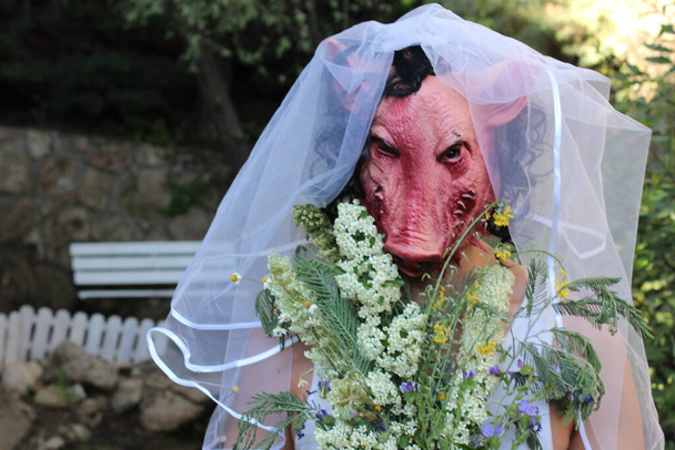 close-up retrato da noiva em máscara de terror com buquê nupcial e vestido em jardim verde - Foto, Imagem