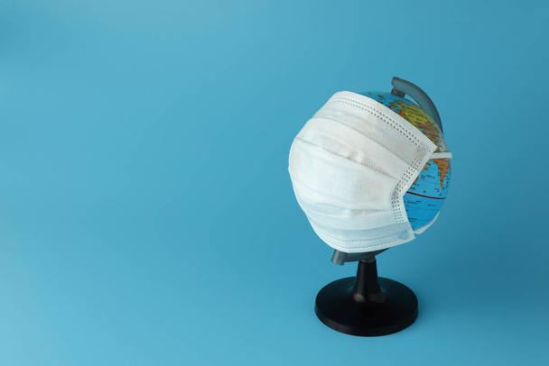 De wereld simulatie met medisch masker voor het stoppen van de verspreiding van het virus op lichtblauwe achtergrond met kopieerruimte. Conceptbestrijding tegen virus. - Foto, afbeelding