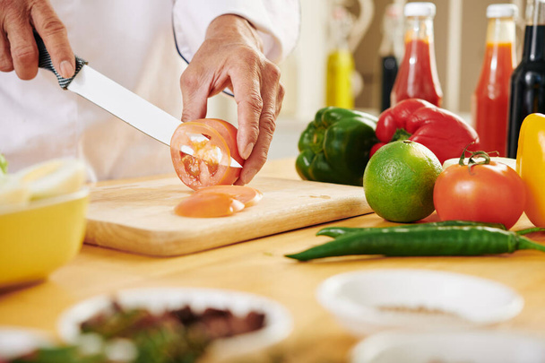 Imagen cercana del hombre maduro cortando tomate en rodajas finas y casi transparentes - Foto, imagen