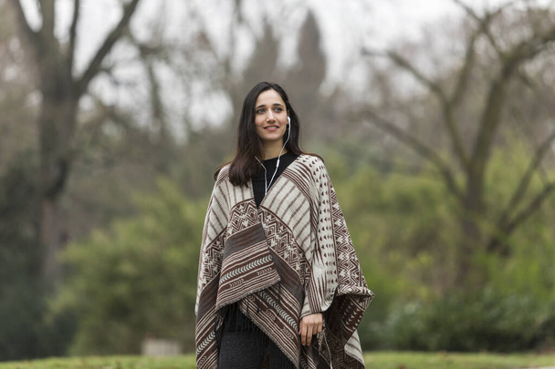 Bella donna indiana vestita in poncho posa all'aperto sorridente e guardando altrove
.  - Foto, immagini