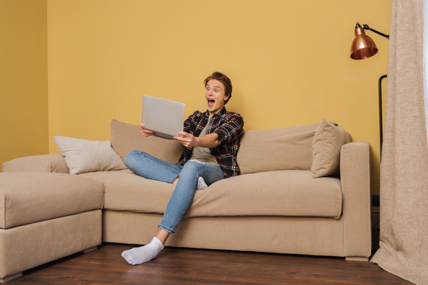 excited freelancer holding laptop in living room  - Foto, afbeelding