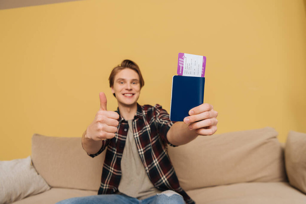 selective focus of cheerful man showing thumb up and holding passport with air ticket, end of quarantine concept  - Photo, Image
