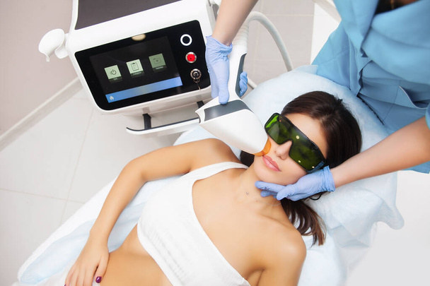 Laser epilation and cosmetology in beauty salon. Hair removal procedure. Laser epilation, cosmetology, spa, and hair removal concept. Beautiful brunette woman remove hair on the upper lip - Fotó, kép